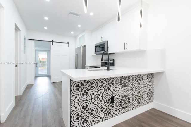 kitchen featuring appliances with stainless steel finishes, a barn door, light countertops, a peninsula, and recessed lighting