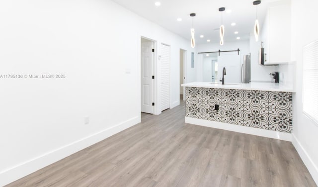 unfurnished living room featuring baseboards, recessed lighting, a barn door, a sink, and light wood finished floors