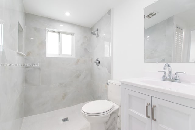 bathroom featuring toilet, visible vents, tiled shower, and vanity