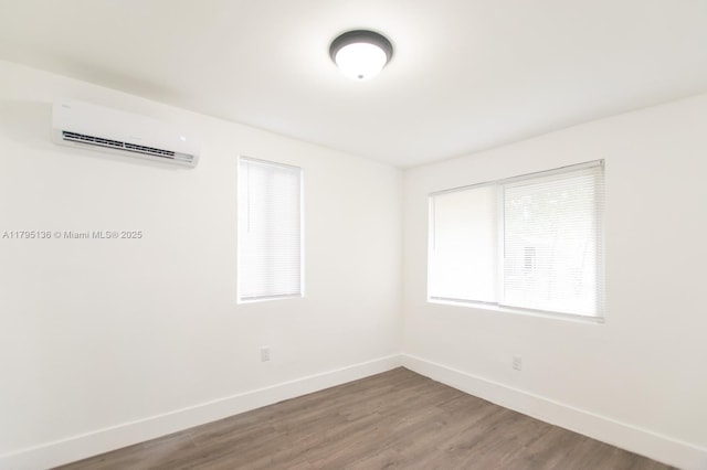 spare room featuring baseboards, a wall unit AC, and wood finished floors