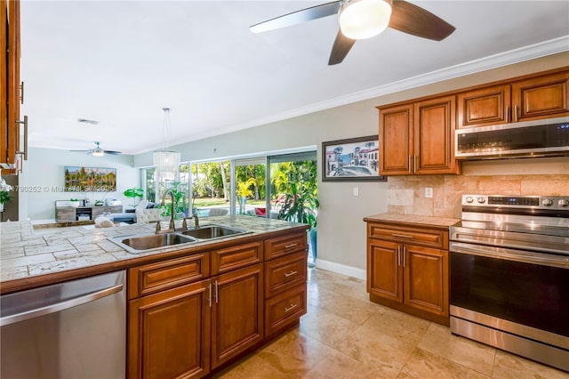 kitchen featuring brown cabinetry, a sink, a ceiling fan, backsplash, and stainless steel appliances