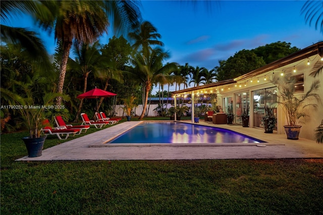 pool at dusk featuring a yard, fence, a fenced in pool, and a patio area