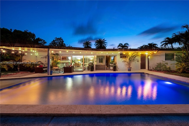 pool at dusk with a patio and an outdoor pool