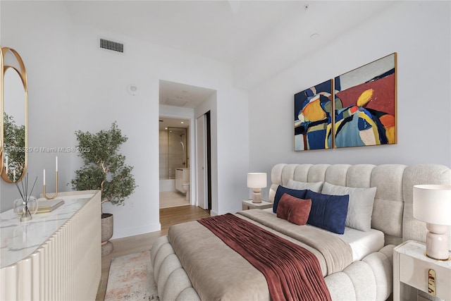 bedroom with baseboards, visible vents, wood finished floors, and ensuite bathroom