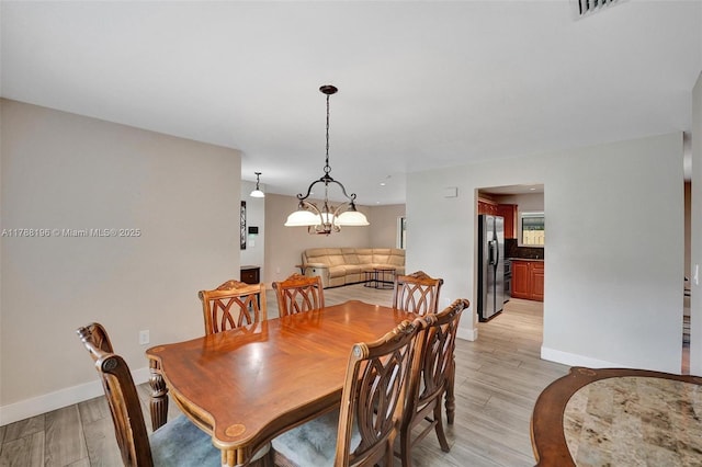 dining space with a notable chandelier, baseboards, visible vents, and light wood-style floors