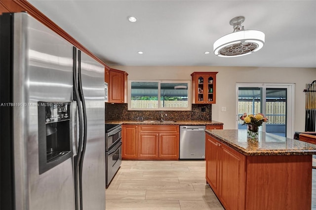 kitchen featuring a kitchen island, appliances with stainless steel finishes, tasteful backsplash, a sink, and dark stone countertops