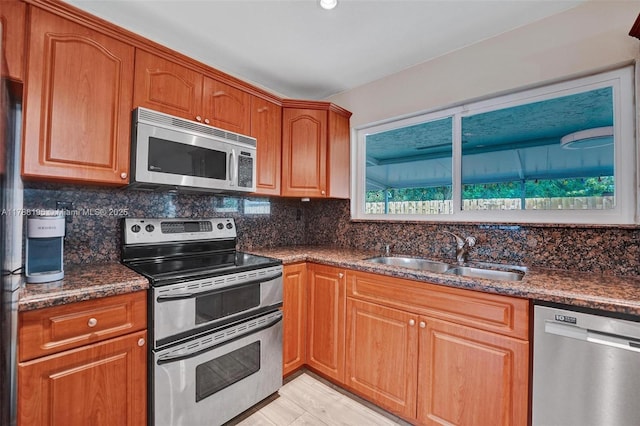 kitchen with a sink, dark stone countertops, backsplash, and stainless steel appliances