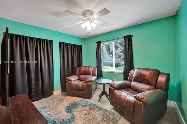 living area featuring a ceiling fan, baseboards, and wood finished floors