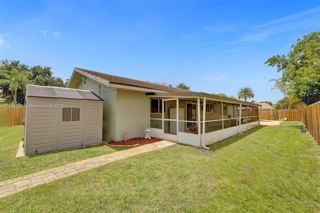 back of house featuring a fenced backyard, stucco siding, a sunroom, a storage unit, and a lawn