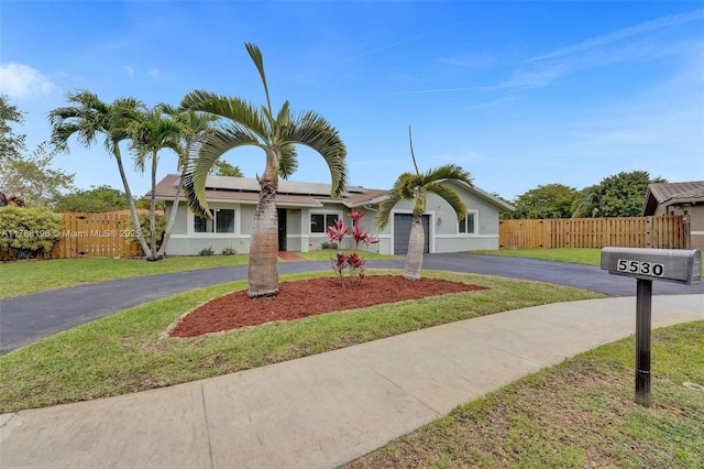view of front of property featuring solar panels, a front yard, a garage, fence, and curved driveway