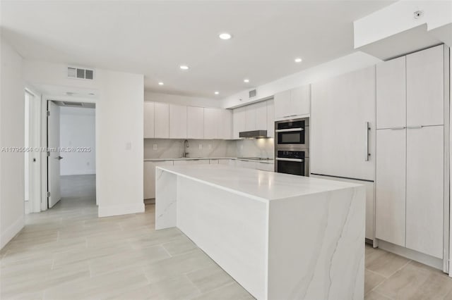 kitchen with a sink, double oven, visible vents, light countertops, and a kitchen island