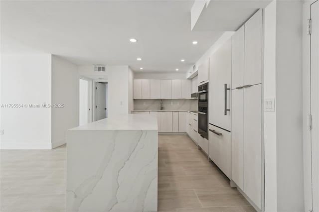 kitchen featuring double wall oven, visible vents, recessed lighting, a center island, and modern cabinets