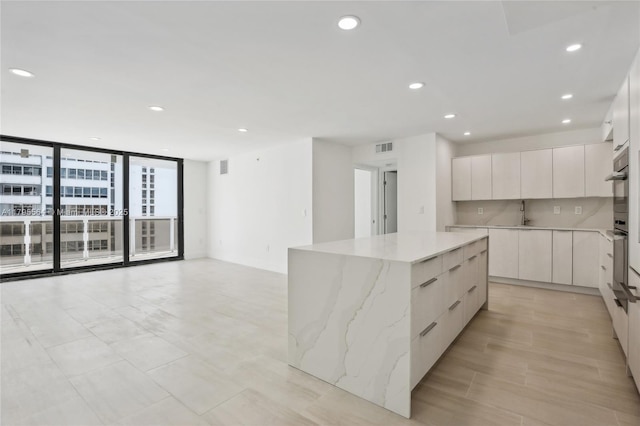kitchen with light stone countertops, recessed lighting, modern cabinets, expansive windows, and a kitchen island