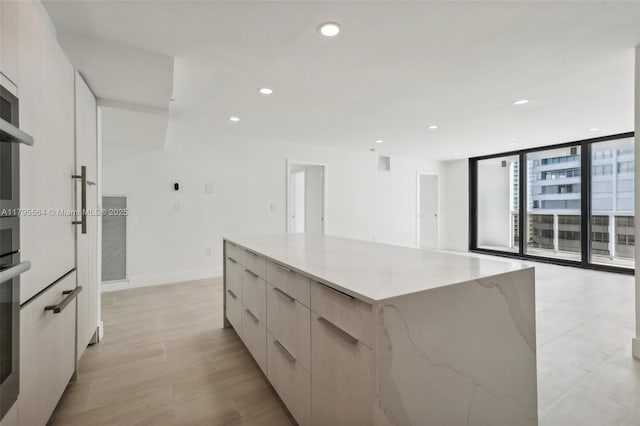 kitchen featuring modern cabinets, a spacious island, recessed lighting, light stone counters, and light wood-style flooring
