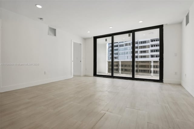 empty room with light wood finished floors, recessed lighting, visible vents, and floor to ceiling windows