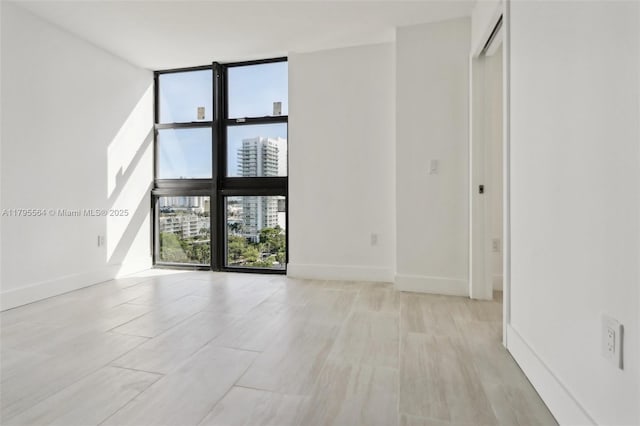 empty room with a city view, light wood finished floors, floor to ceiling windows, and baseboards