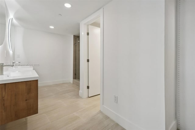 bathroom featuring a stall shower, recessed lighting, baseboards, a sink, and double vanity