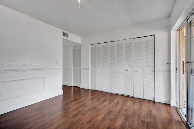 unfurnished bedroom featuring a textured ceiling, visible vents, wood finished floors, and a closet