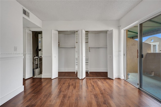 unfurnished bedroom with a textured ceiling, access to exterior, visible vents, wood finished floors, and two closets