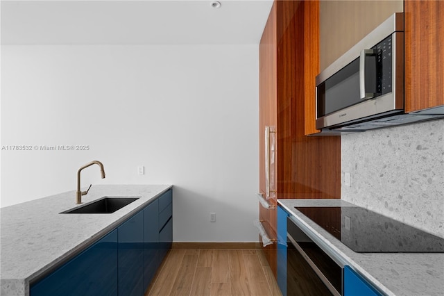 kitchen with a sink, black electric cooktop, blue cabinetry, stainless steel microwave, and decorative backsplash