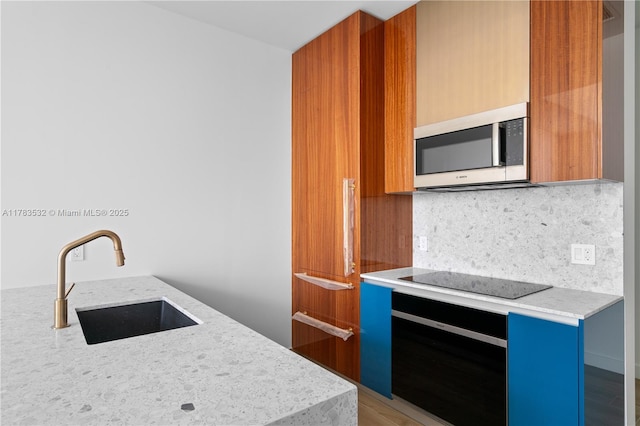 kitchen featuring wall oven, modern cabinets, black electric stovetop, stainless steel microwave, and a sink