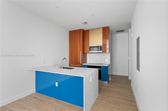 kitchen featuring a sink, a peninsula, stainless steel microwave, decorative backsplash, and visible vents