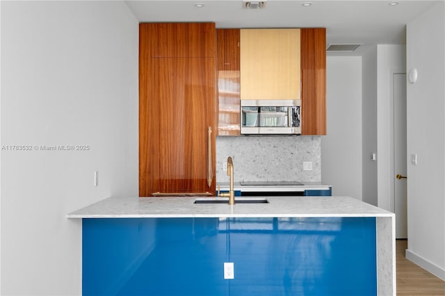 kitchen with brown cabinets, a sink, stainless steel microwave, wood finished floors, and tasteful backsplash