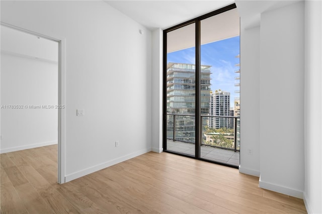 spare room featuring a city view, wood finished floors, a healthy amount of sunlight, and a wall of windows
