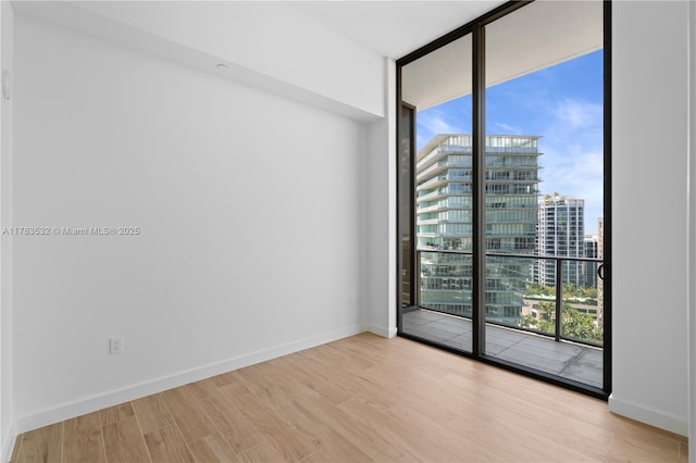 spare room featuring baseboards, floor to ceiling windows, a city view, and wood finished floors