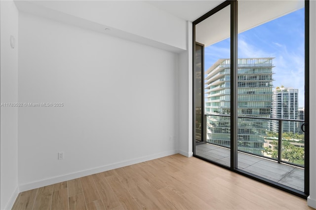 empty room featuring a view of city, floor to ceiling windows, a healthy amount of sunlight, and wood finished floors