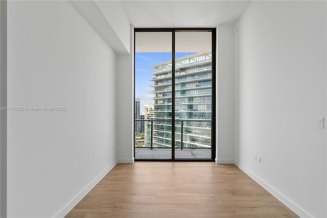 spare room featuring expansive windows, light wood-style floors, and baseboards