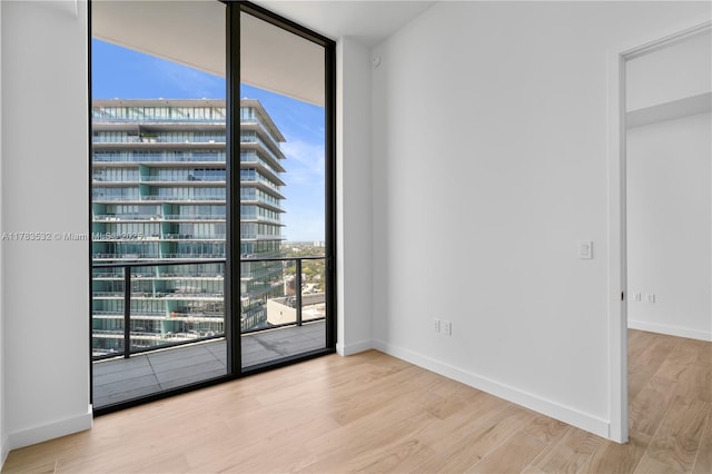 spare room featuring baseboards, a wall of windows, and wood finished floors