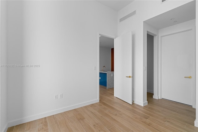 unfurnished room with visible vents, a sink, light wood-style floors, and baseboards