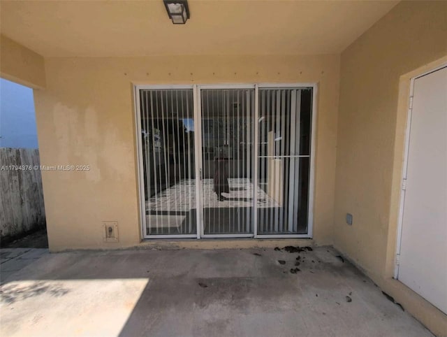 entrance to property with fence, stucco siding, and a patio area
