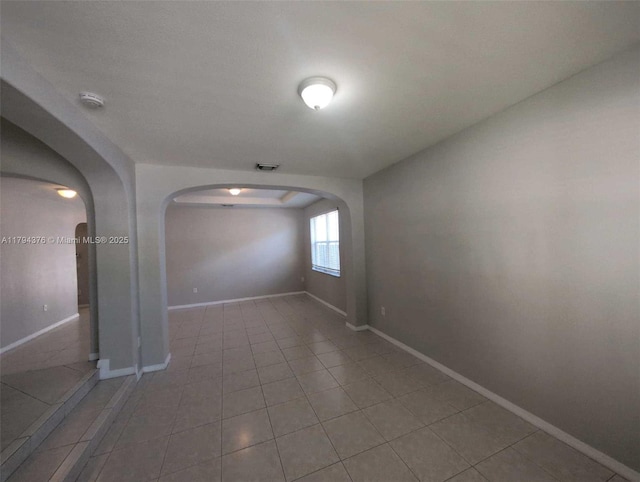 tiled spare room with arched walkways, baseboards, and visible vents