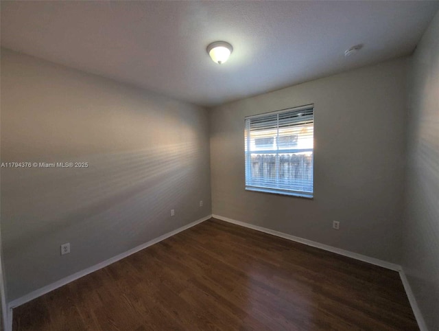 unfurnished room featuring baseboards and dark wood-type flooring