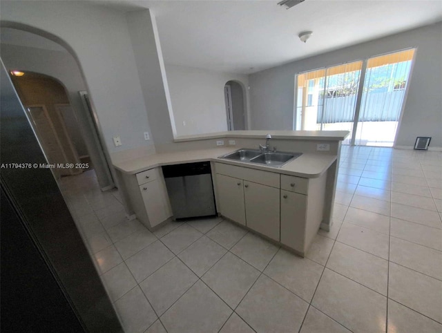 kitchen featuring arched walkways, dishwasher, a sink, light countertops, and light tile patterned flooring