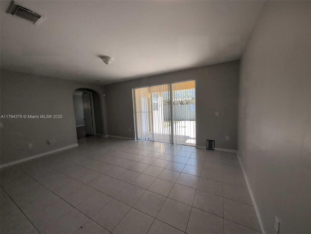 spare room featuring light tile patterned floors, arched walkways, baseboards, and visible vents