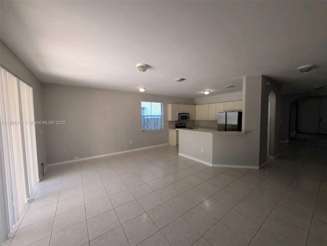 unfurnished living room with arched walkways, baseboards, and light tile patterned floors