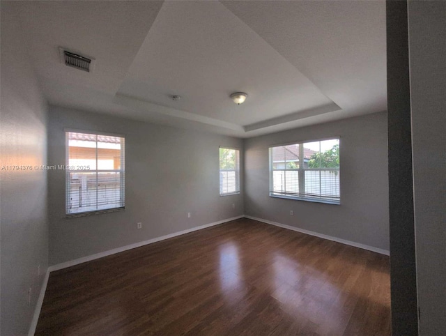 spare room with visible vents, a raised ceiling, baseboards, and dark wood-style floors