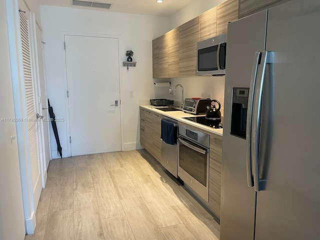 kitchen featuring light countertops, stainless steel appliances, light wood finished floors, and a sink
