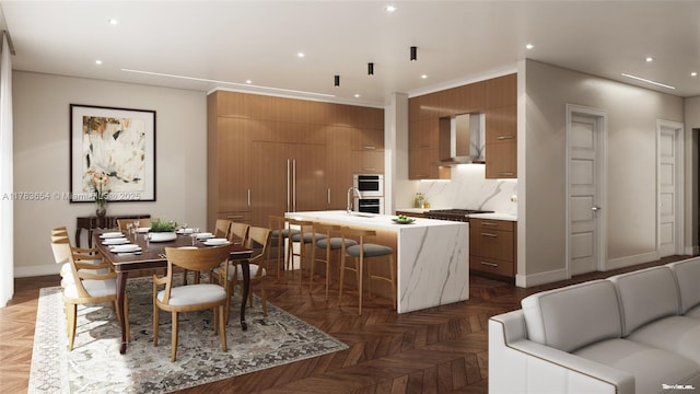 626 Malaga Ave, Coral Gables, FL 33134 - kitchen with wall chimney exhaust hood, brown cabinets, light countertops, modern cabinets, and a kitchen island with sink