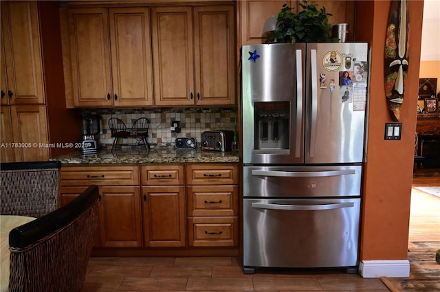 kitchen with stainless steel fridge, dark stone counters, decorative backsplash, and brown cabinets
