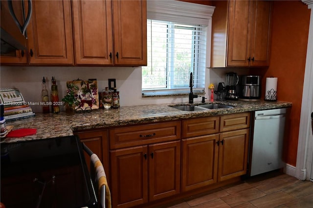 kitchen with dark stone countertops, brown cabinetry, a sink, and dishwasher