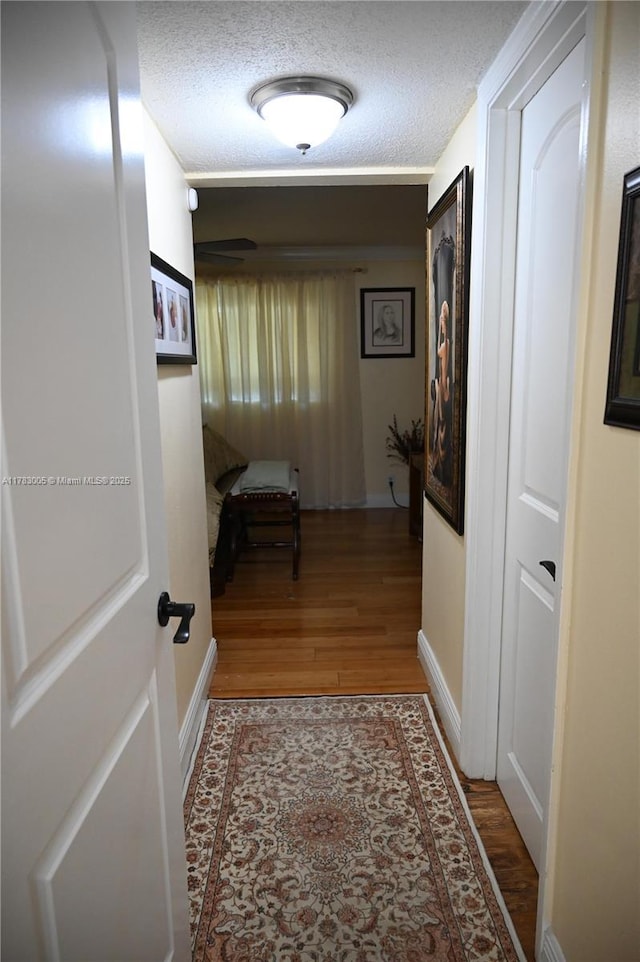 corridor featuring baseboards, a textured ceiling, and wood finished floors