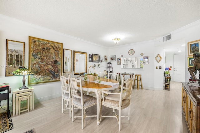 dining area with crown molding, a textured ceiling, visible vents, and light wood finished floors