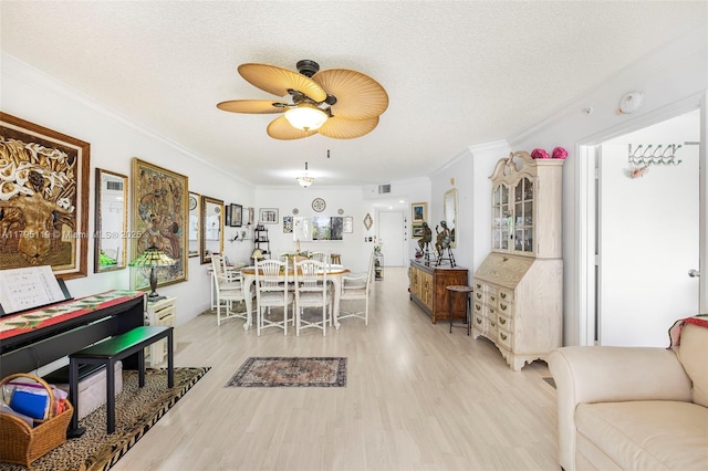 interior space with light wood-style floors, ceiling fan, ornamental molding, and a textured ceiling