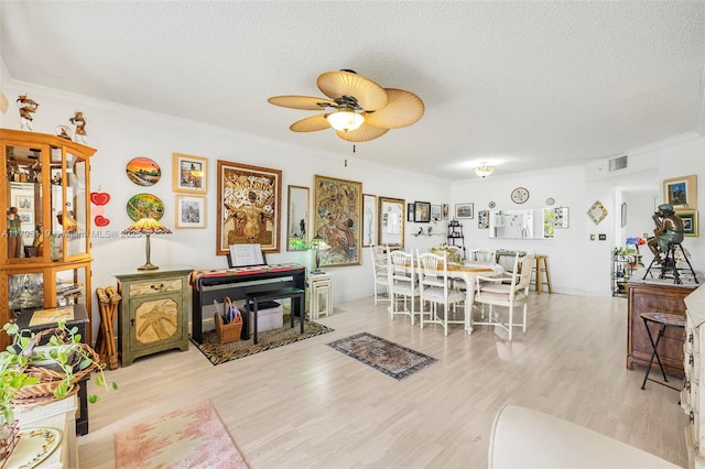 living area featuring crown molding, ceiling fan, a textured ceiling, wood finished floors, and visible vents