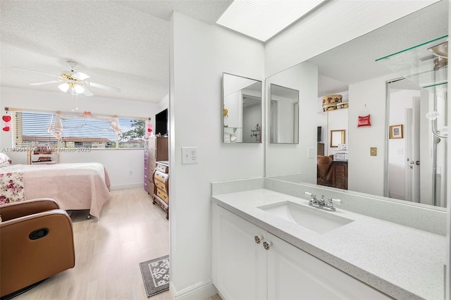 ensuite bathroom with connected bathroom, ceiling fan, vanity, a textured ceiling, and wood finished floors