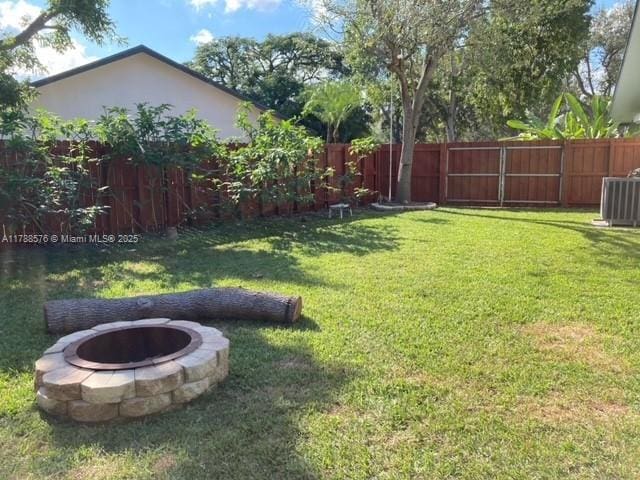 view of yard with central AC, a fenced backyard, and an outdoor fire pit